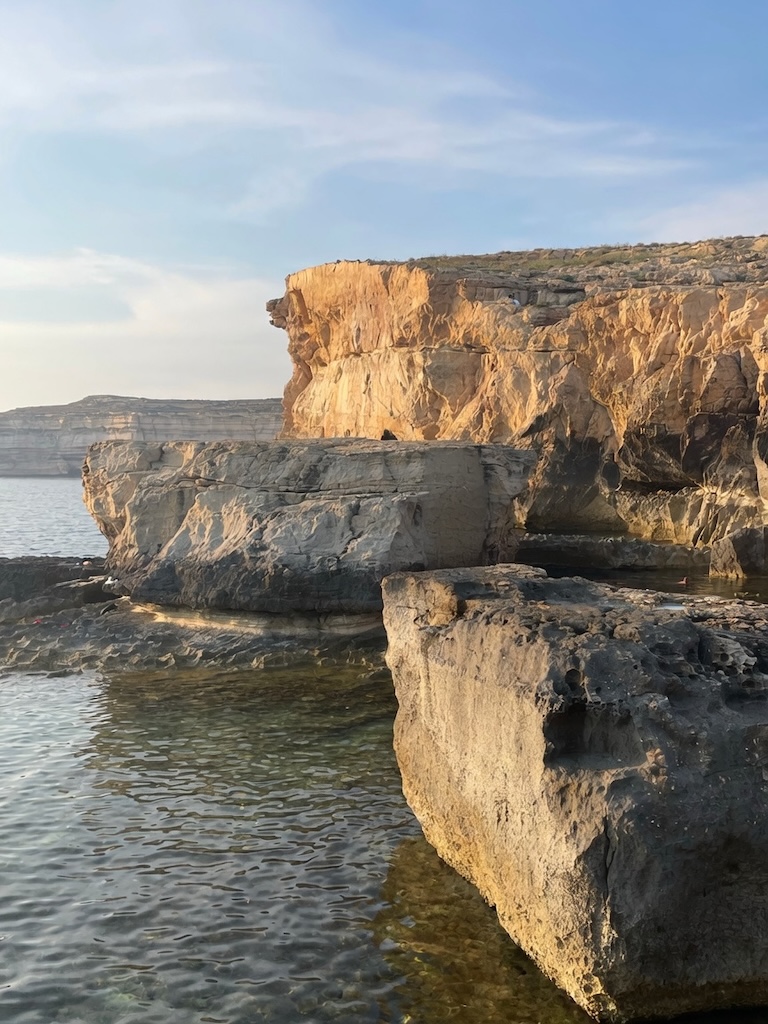 The dramatic golden limestone cliffs and rock formations at Dwejra, Gozo, above clear shallow water at sunset